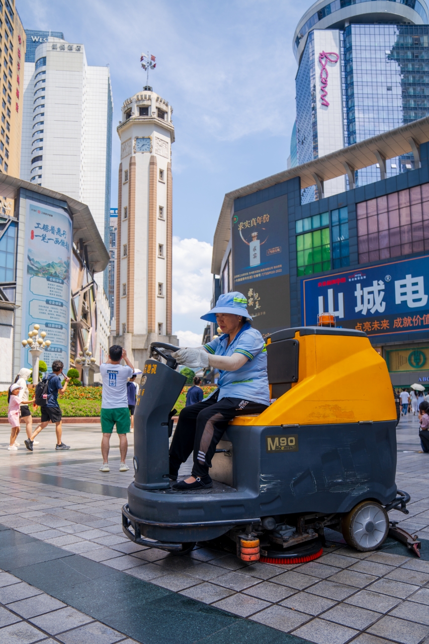 在解放碑,滚滚热浪迎面扑来,环卫工人驾驶智能清扫设备缓缓移动,身后又是一片洁净。